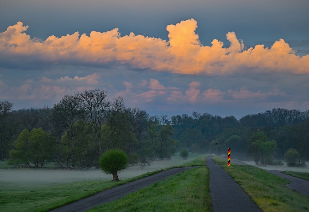 Der Sonnenaufgang scheint auf Wolken über dem Oder-Neiße-Radweg am Deich nahe dem deutsch-polnischen Grenzfluss Oder.