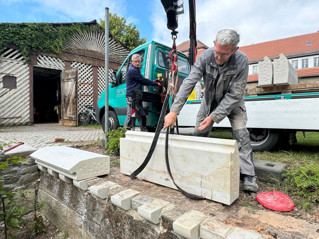 Mitarbeiter eines Steinmetzbetriebs setzen die ersten Sandsteinelemente für den neuen Zaun am Schloss Möckern.