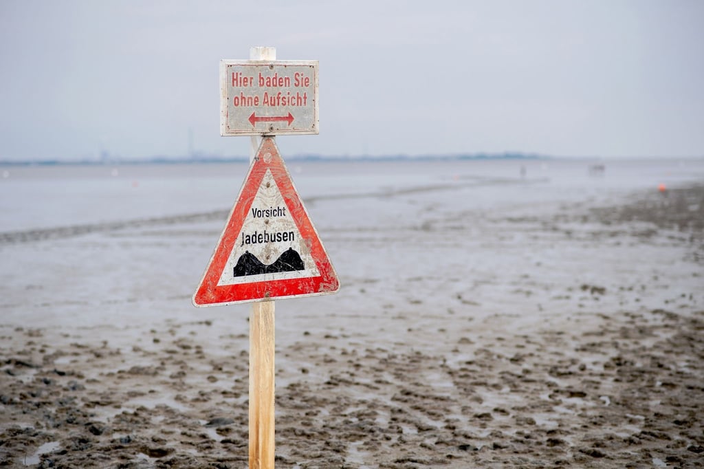 Ein Schild mit der Aufschrift "Vorsicht Jadebusen" steht im Wattboden am Strand von Dangast.