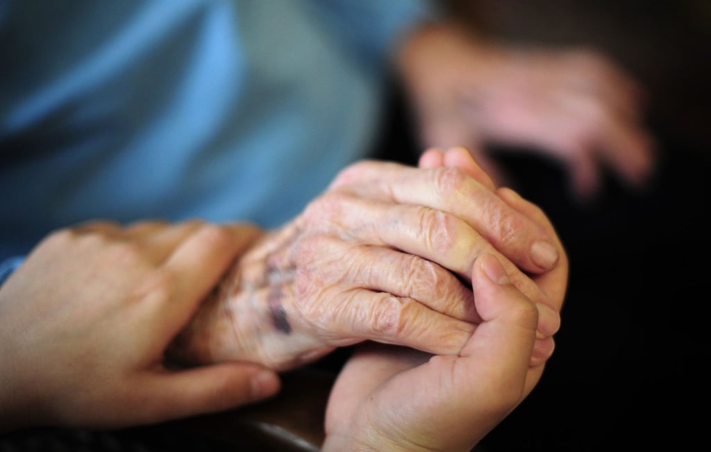 Eine Pflegekraft hält in einem Seniorenheim die Hand einer Bewohnerin. Die Pflegeversicherung sieht sich mit einem Defizit konfrontiert.
