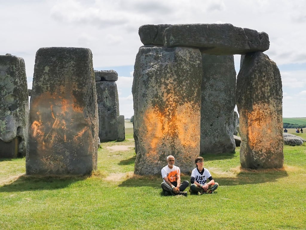 Demonstranten von „Just Stop Oil“ sitzen vor dem Steinmonument Stonehenge, das sie zuvor mit orangener Farbe besprüht haben.