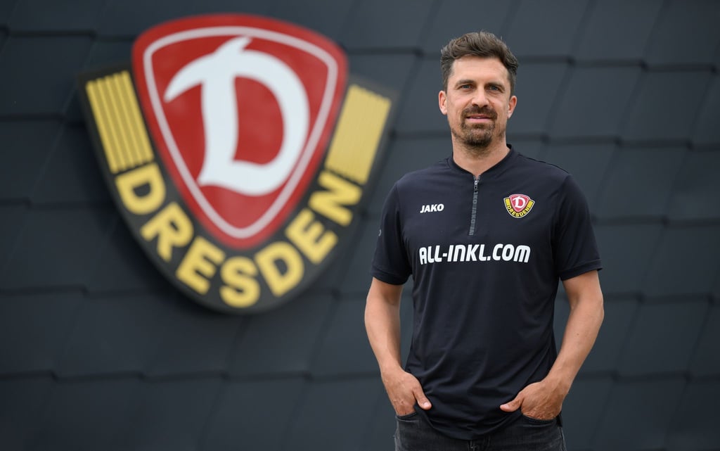 Thomas Stamm, neuer Trainer des Fußball-Drittligisten SG Dynamo Dresden, steht nach seiner Vorstellung in der Trainingsakademie vor dem Logo des Vereins.