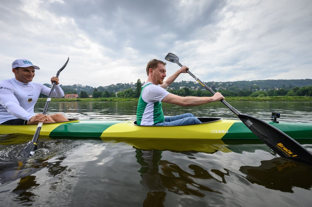 Michael Kretschmer (CDU, r), Ministerpräsident von Sachsen, und Tom Liebscher-Lucz, Doppel-Olympiasieger im Kanu, sitzen in einem Zweierkajak und paddeln auf der Elbe.