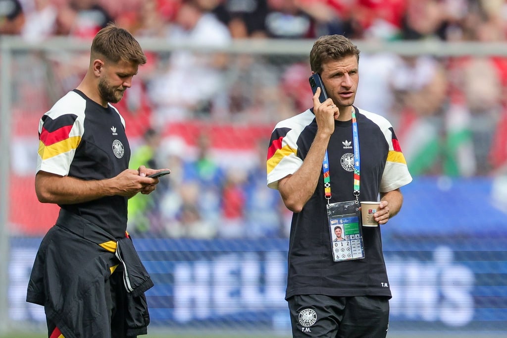 Deutschlands Thomas Müller (r) steht telefonierend mit einem Getränk auf dem Rasen, neben ihm Niclas Füllkrug.