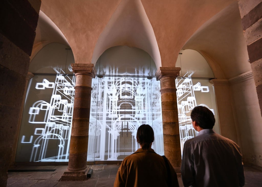 Vertreter des Presseteams stehen nach der Pressekonferenz vor der Medienwand im Unesco-Welterbe Corvey auf der eine 3D-Animation des Westwerks zu sehen ist.