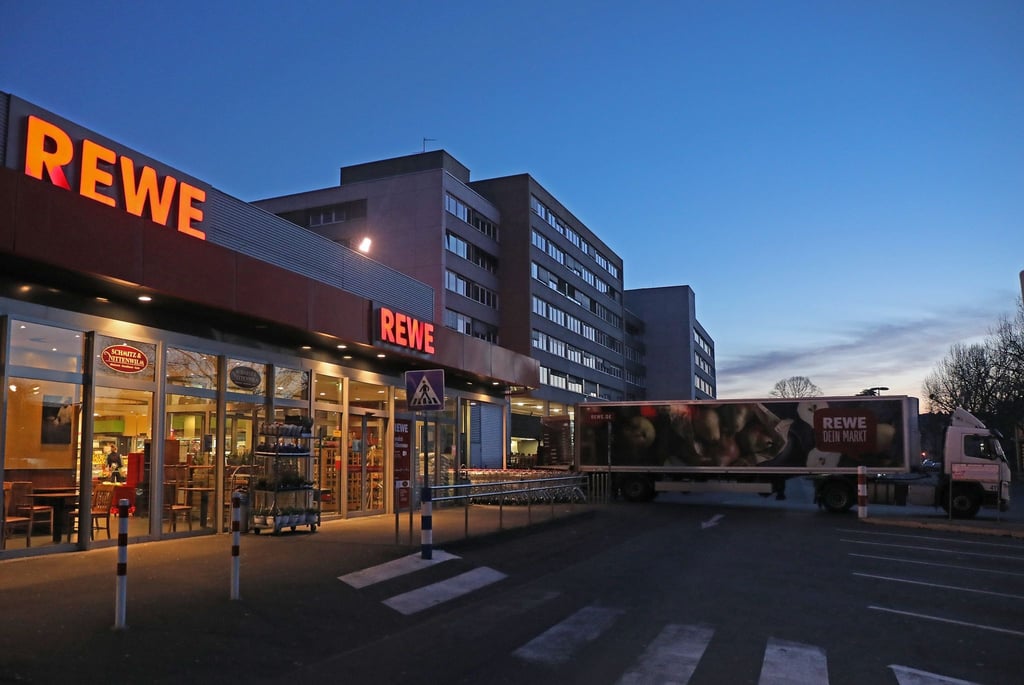Ein Lkw steht am frühen Morgen vor einem Rewe Supermarkt, der mit Waren beliefert wird.