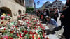 Menschen stehen am Rande eines Gottesdienstes für die getötete Valeriia auf dem Obermarkt vor Blumen und Kerzen.
