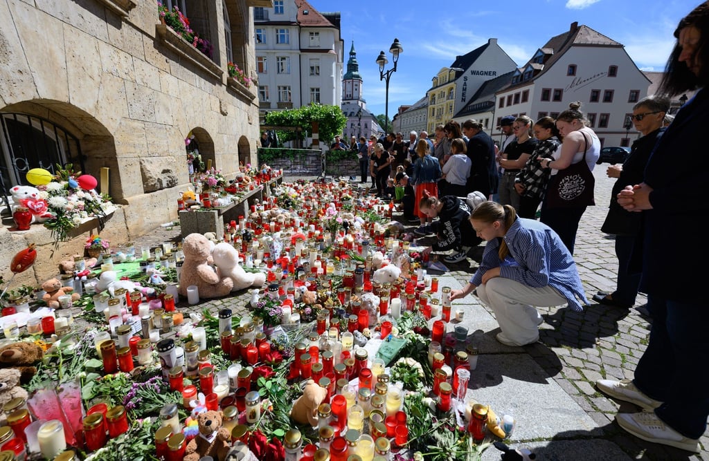 Menschen stehen am Rande eines Gottesdienstes für die getötete Valeriia auf dem Obermarkt vor Blumen und Kerzen.