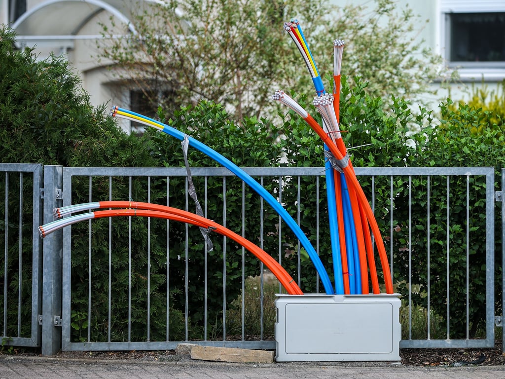 Aus dem Sockel eines Schaltschranks ragen Glasfaserkabel heraus.
