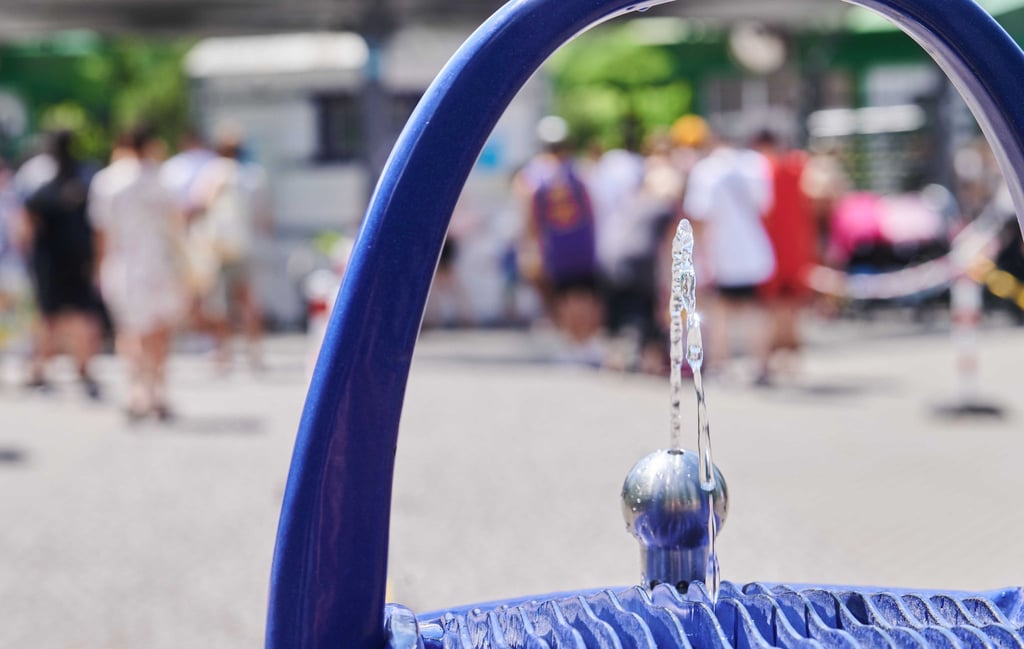 An einem Freibad in Berlin stehen die Menschen Schlange, während man davor Wasser an einer öffentlichen Wasserstelle trinken kann.