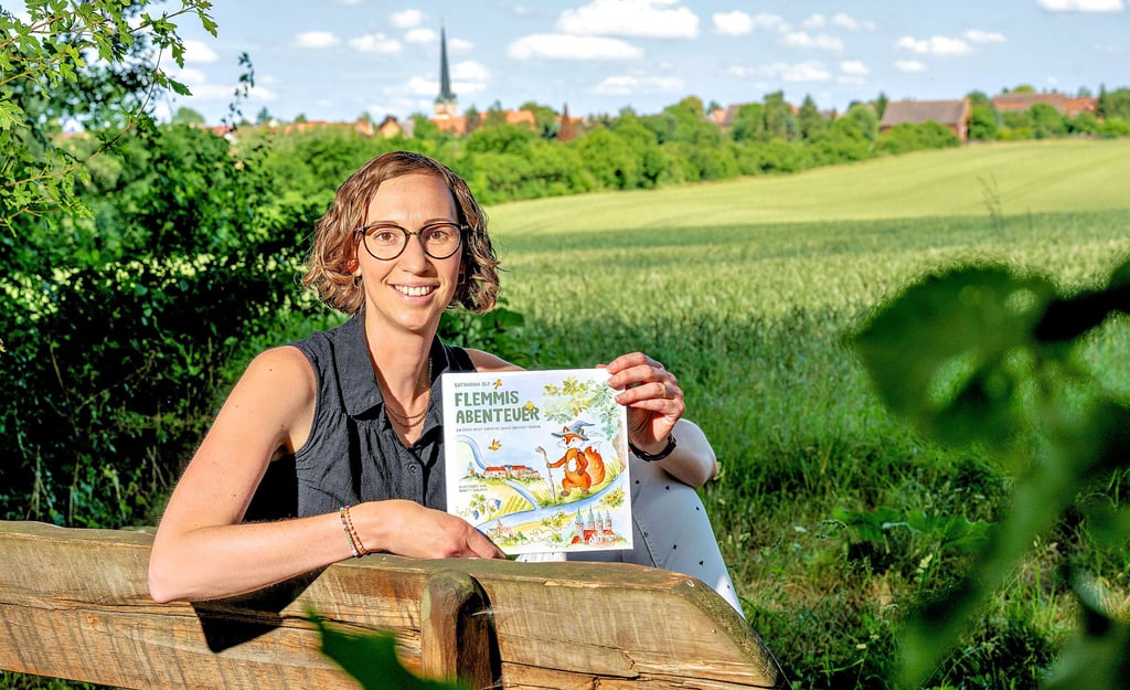 Katharina Alf mit ihrem Kinderbuch „Flemmis Abenteuer“, das in die Saale-Unstrut-Region führt. Im Hintergrund: Flemmingen.