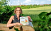 Katharina Alf mit ihrem Kinderbuch „Flemmis Abenteuer“, das in die Saale-Unstrut-Region führt. Im Hintergrund: Flemmingen.  