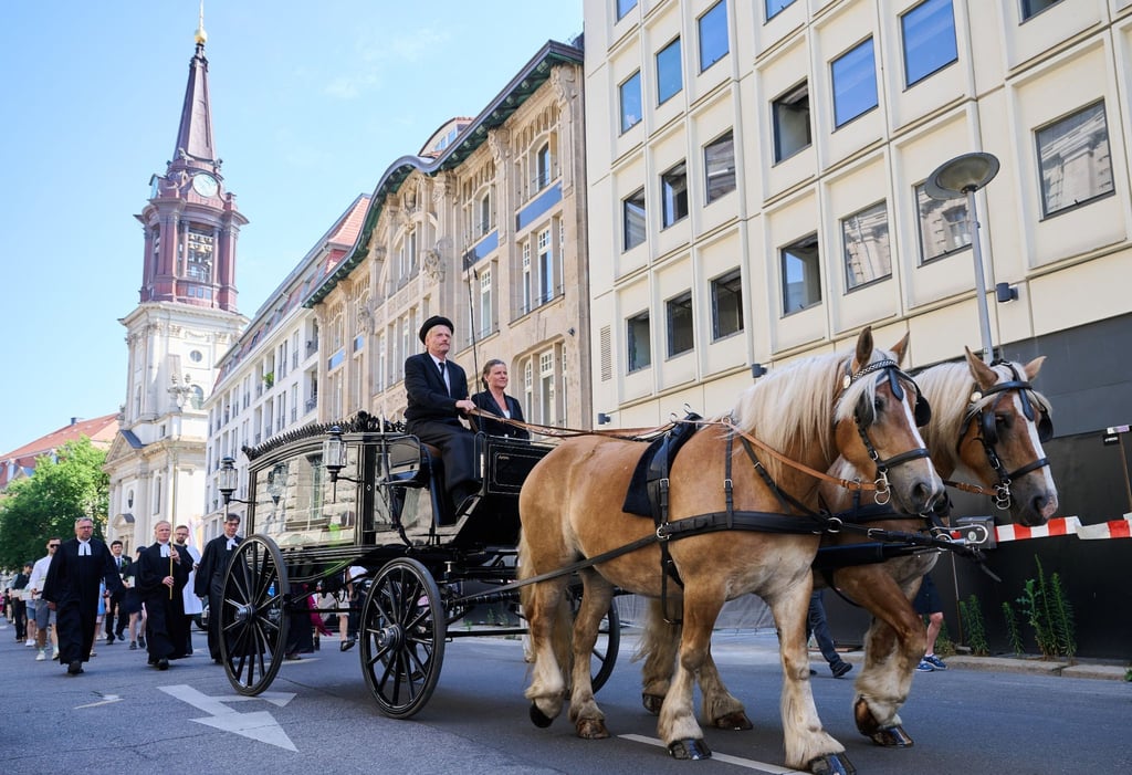 Eine Prozession, in der Kinder und Erwachsene die Gebeine der ersten mittelalterlichen und frühneuzeitlichen Berlinerinnen und Berliner in kleinen Särgen von der Parochialkirche zum Petriplatz tragen, wird von einer Kutsche und Geistlichen angeführt.