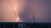 Ein Blitz entlädt sich während eines Gewitters hinter dem Fernmeldeturm Telemax.