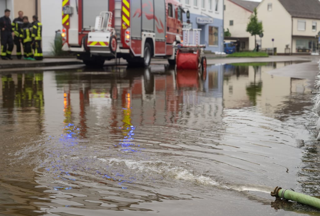 Aus einem Schlauch wird Wasser aus einem Keller auf eine überflutete Straße gepumpt.