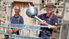 Jörg Otto (rechts) und sein Mitarbeiter Friedrich Weigert von der Metallwerkstatt Otto aus Halle mit der neuen Wetterfahne und der Turmkugel. 