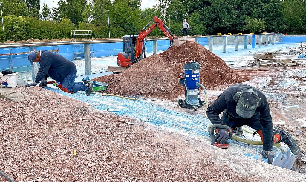 Mühsam und mit Hand wird die blaue Farbe vom Beton entfernt.