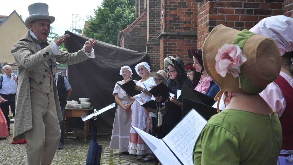 Biedermeier-Sommermarkt 2024 in Werben (Elbe), Landkreis Stendal: An hellen Tagen, Herz, welch’ ein schlagen - der Gemische Chor Werben unter Leitung von Jochen Großmann eröffnete den Markt. Natürlich „gut behütet“.