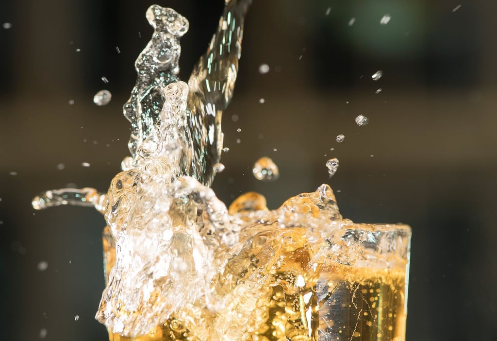 ILLUSTRATION: Apfelschorle spritzt aus einem Glas.
