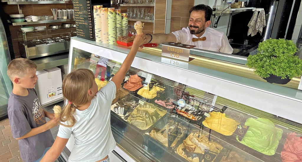 Dashmir Miniri vom „Eiscafé Orient“ reicht Snickers-Eis an Bennet und Élise über die Ladentheke.