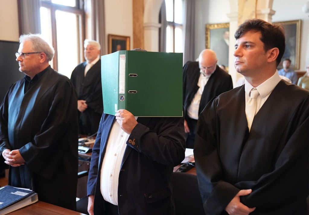 Ein Angeklagter verdeckt im Hamburger Landgericht sein Gesicht mit einem Ordner. Zwei Lieferanten und ein Materialprüfer sollen den Hamburger Kupferhersteller Aurubis um Millionen betrogen haben.