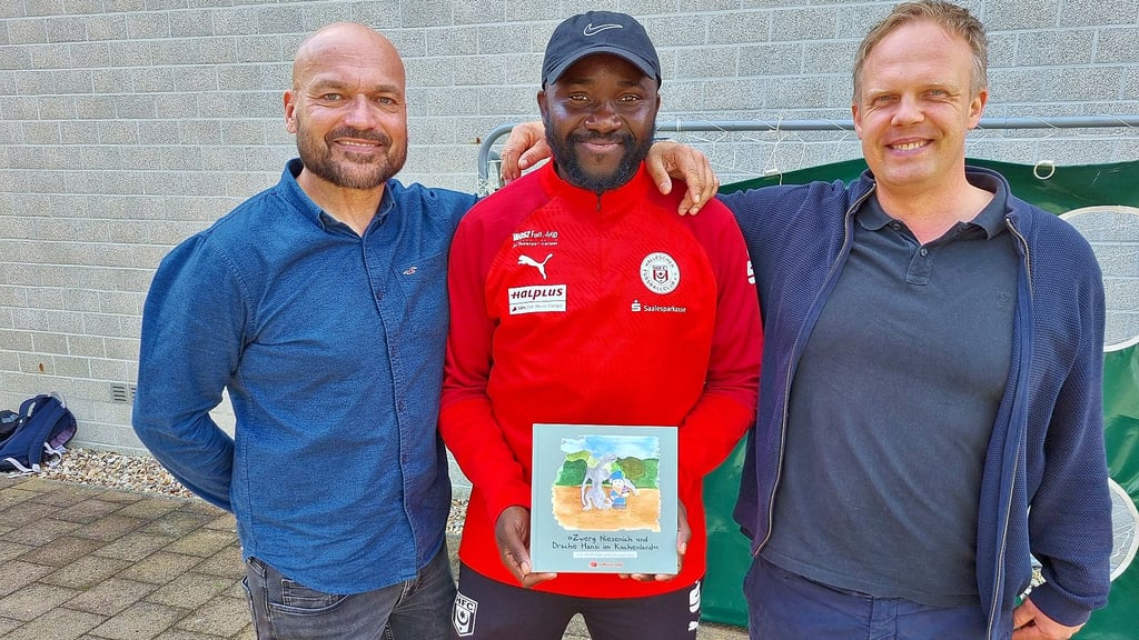 Autor Jan Putzas (l.) und Künstler Christian Doil (r.) präsentieren gemeinsam mit HFC-Ex-Profi Patrick Mouaya an der Berufsschule in Köthen ihr Kinderbuch.