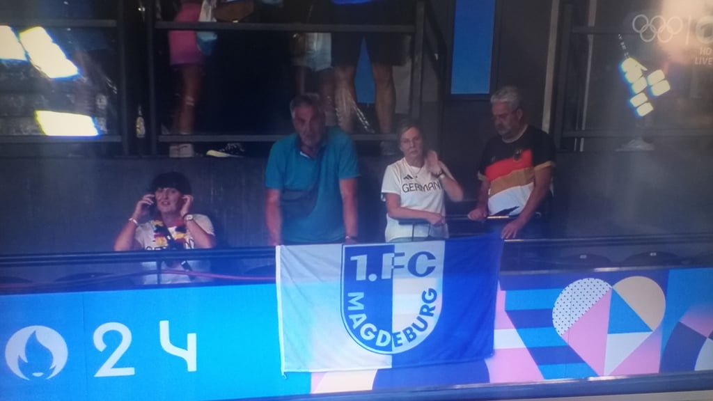 FCM-Fahne Olympia live im TV vor Millionen Zuschauern in der ARD: Links telefoniert kurz vor dem Start noch Lukas Märtens' Mutter, rechts daneben sein Onkel Thomas mit der FCM-Fahne aus dem heimischen Magdeburg.