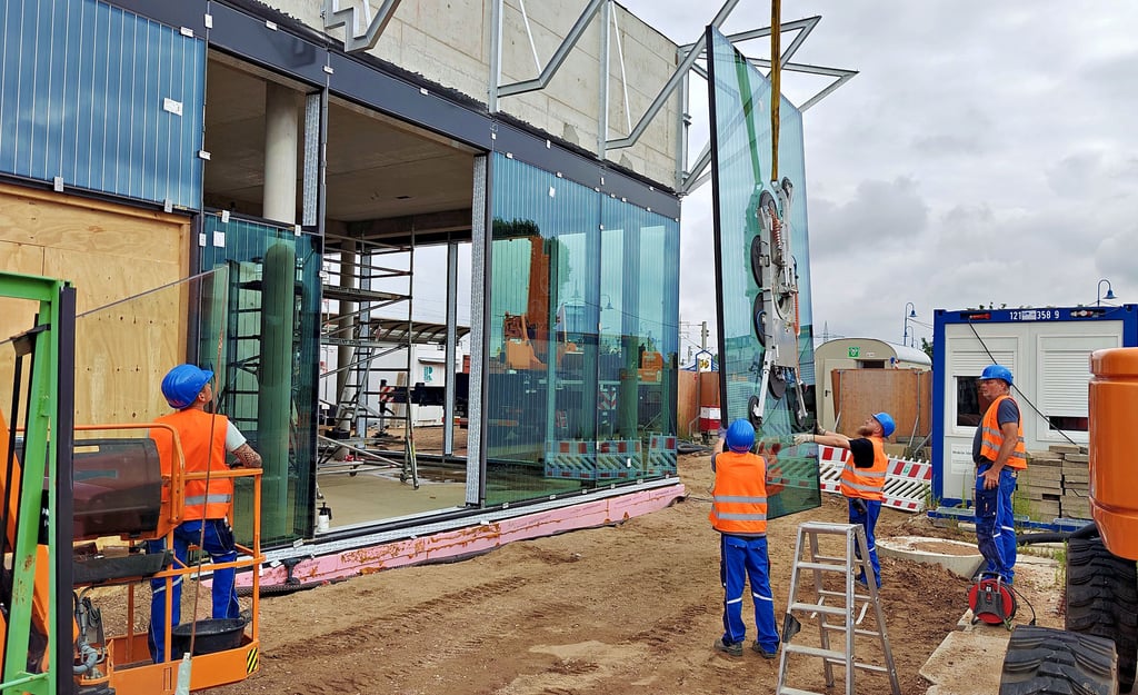 Stück für Stück werden die mit Saugtellern am Kran hängenden großen Glasscheiben in die Fassadenfront eingefügt.