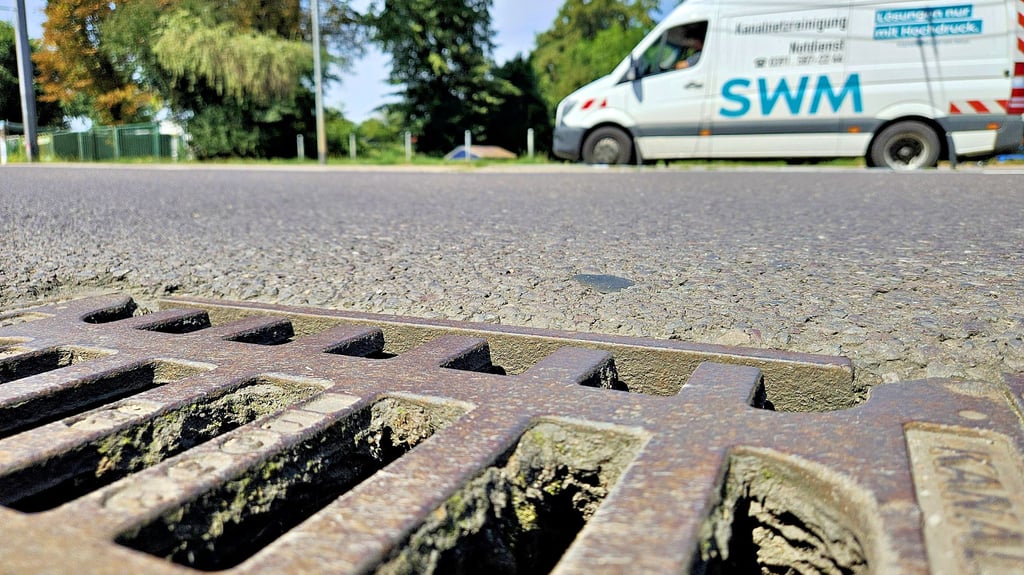Blick über einen Gully auf dem  Schöppensteg in Höhe Vogelgesangpark in Magdeburg. Im Hintergrund passiert ein Fahrzeug der SWM-Kanalnetzreinigung die Stelle.