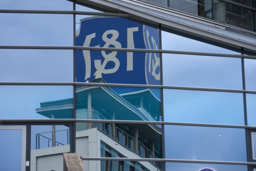 Das 1&1-Firmenlogo auf dem Dach eines Firmengebäudes spiegelt sich in einer Glasfassade.