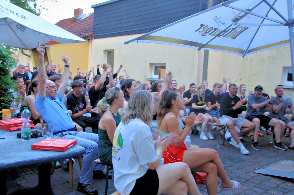 Aktive Spieler des Cöthener HC, Freunde und andere Vereinsmitglieder feiern vor dem Sportlerheim den deutschen Sieg gegen Indien.