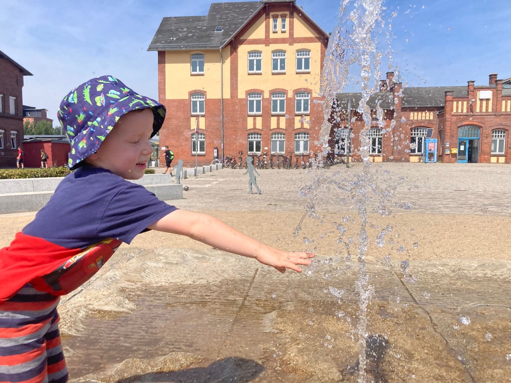 Es plätschert am Bahnhofsvorplatz in Burg. Die Wasserfontänen sind eine willkommene Abkühlung, nicht nur für den kleinen Lukasz.
