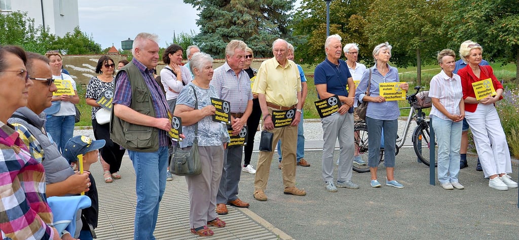 Teilnehmer der Gedenkveranstaltung mit Bürgermeister René Zok (CDU) am Staßfurter Friedenspfahl anlässlich der Atombombenabwürfe vor 79 Jahren in Japan. „Atomwaffen abschaffen!“ mahnen sie auf den Handplakaten.