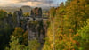 Sonnenlicht fällt am Morgen auf die herbstlich gefärbten Bäume im Nationalpark Sächsische Schweiz nahe der Basteibrücke. (Archivbild)