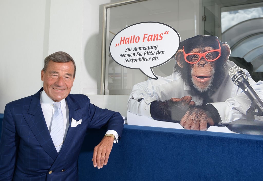 Wolfgang Grupp senior mit einem Werbeschild, auf dem der bekannte Werbe-Affe "Charly" abgebildet ist.
