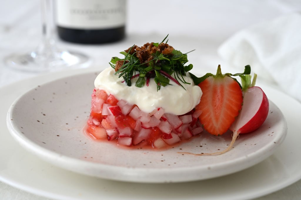 Der Erdbeer-Radieschen-Salat wird mit einem Servierring in Form gebracht. Darauf gibt es als Topping Ziegen-Feta-Creme, Kräutersalat und geröstete Krümel vom Schwarzbrot. Serviert wird er mit einem alkoholfreien Rosé.