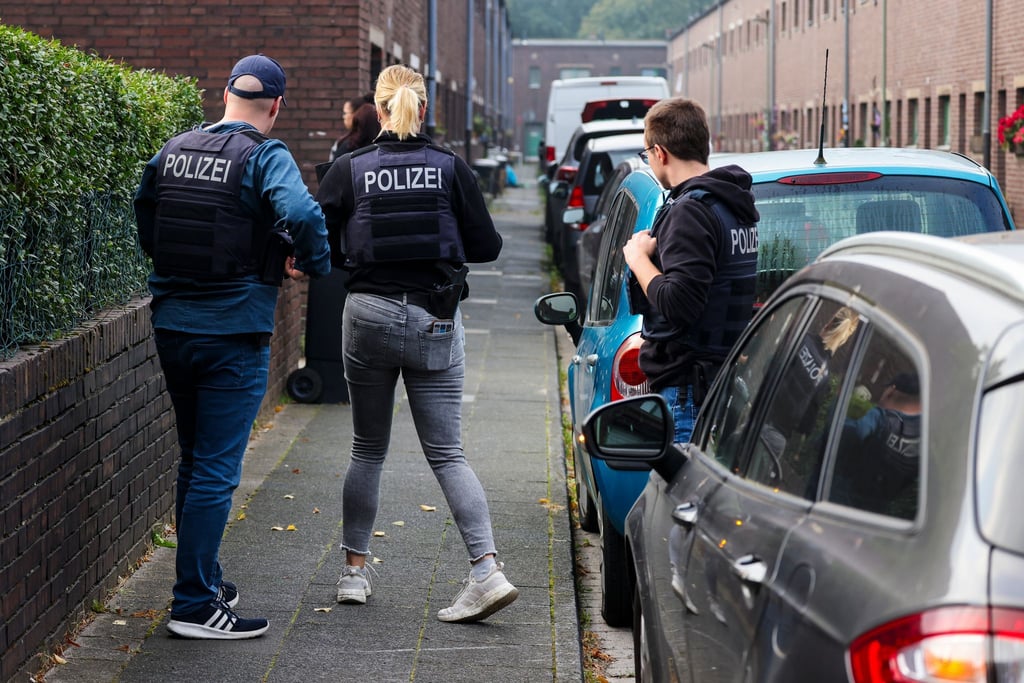 Beamte der Polizei stehen auf einer Straße vor einem Haus in Duisburg, das gerade durchsucht wird.