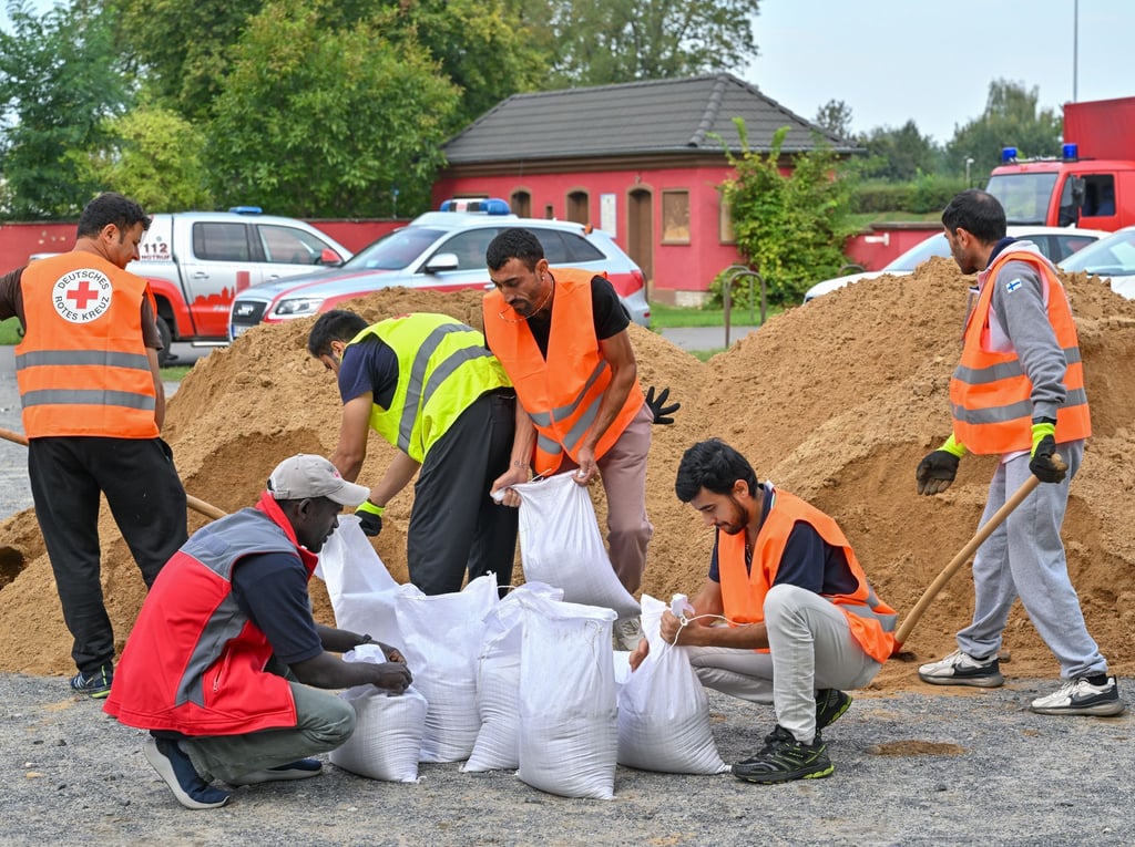 Nach einem Aufruf zur freiwilligen Mithilfe sind Menschen aus einer Unterkunft der Zentralen Ausländerbehörde an Sandsäcken im Einsatz.