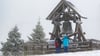 Zwei Wanderer stehen vor der Friedensglocke auf dem Fichtelberg. (Archivbild)