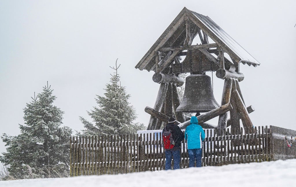 Zwei Wanderer stehen vor der Friedensglocke auf dem Fichtelberg. (Archivbild)