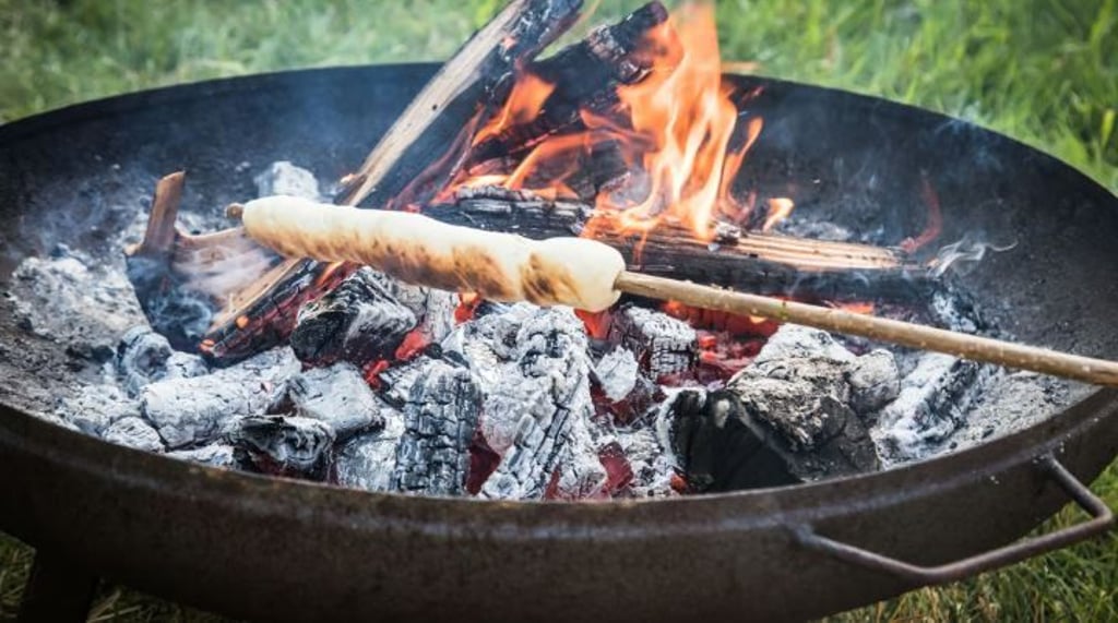 Ein einfacher Hefeteig ist um einen Haselnuss-Stock gewickelt und wird über dem Lagerfeuer gebacken. 