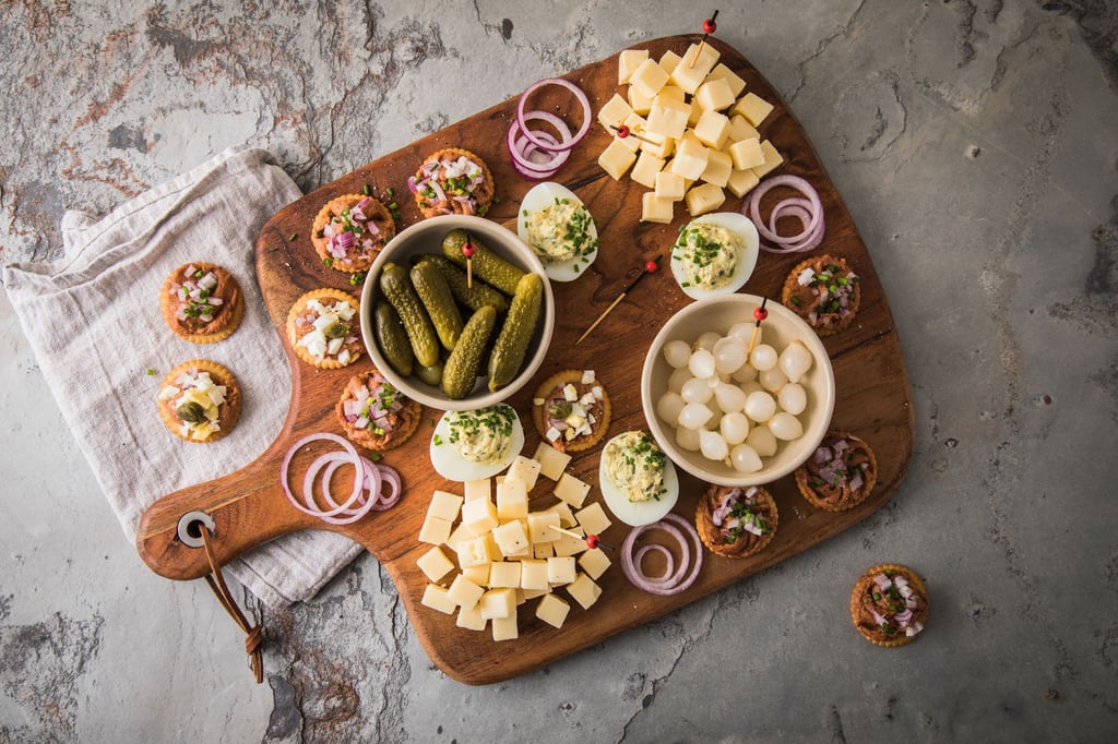 Eine typische niederländische Borrel-Platte mit Filet Americain auf Crackern mit Zwiebel, Ei oder Kapern. Dazu werden Käsewürfel, Cornichons, Silberzwiebeln und gefüllte Eier mit Schnittlauch serviert.