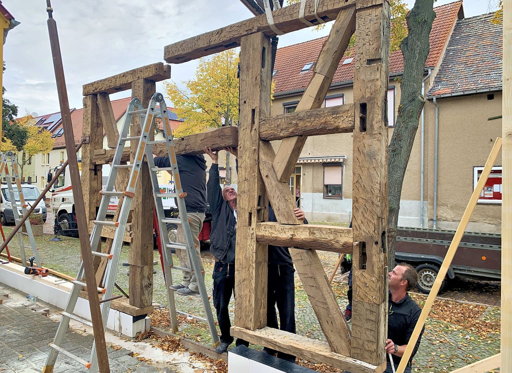 Mitarbeiter der Zimmerei Uhlemann fügen die beiden Teile des Portals zusammen. Die rechte Seite hängt noch am Haken des Krans.