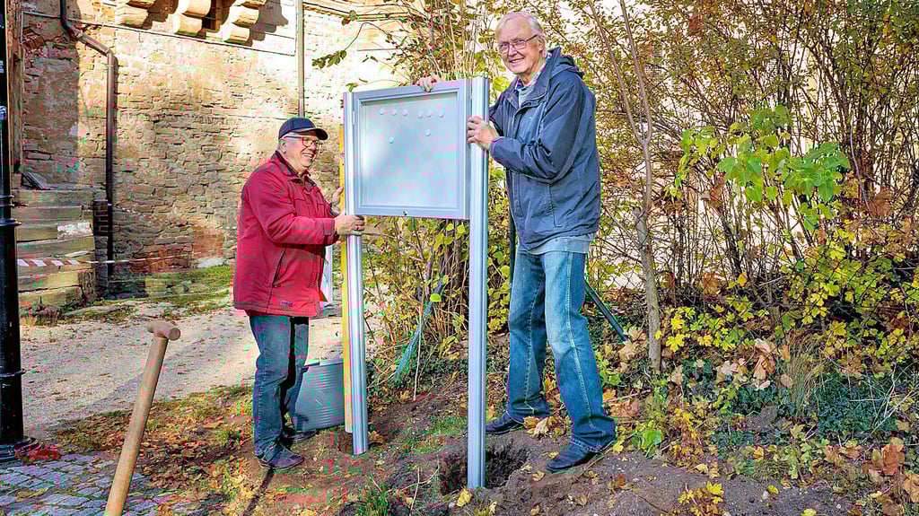 Helmut Gottwald und Horst Vandreicke vom Droyßiger Schlossverein stellen eine Infotafel vor der Kapelle auf.