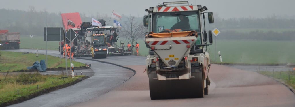 Mit wehenden Fahnen asphaltieren die Strabag-Leute mit ihren Maschinen – der Fertiger im Hintergrund auf einer Breite von sieben Metern – die Landesstraße 73. In dieser Woche soll der neue Asphalt zwischen Hohenerxleben und Neugattersleben komplett sein.