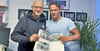 Hartmut Schulz (links) und Mark Wilke mit dem Buch „Tangerhütter Schulen“ von Albrecht Will, in dem auch ein Faschingsfoto ihrer Klasse aus den 80ern zu finden ist.