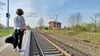 Eine Person mit Reisetasche späht am Bahnsteig 1 des Haltepunktes Gnadau nach einem Zug, der aus Richtung Schönebeck erwartet wird. 