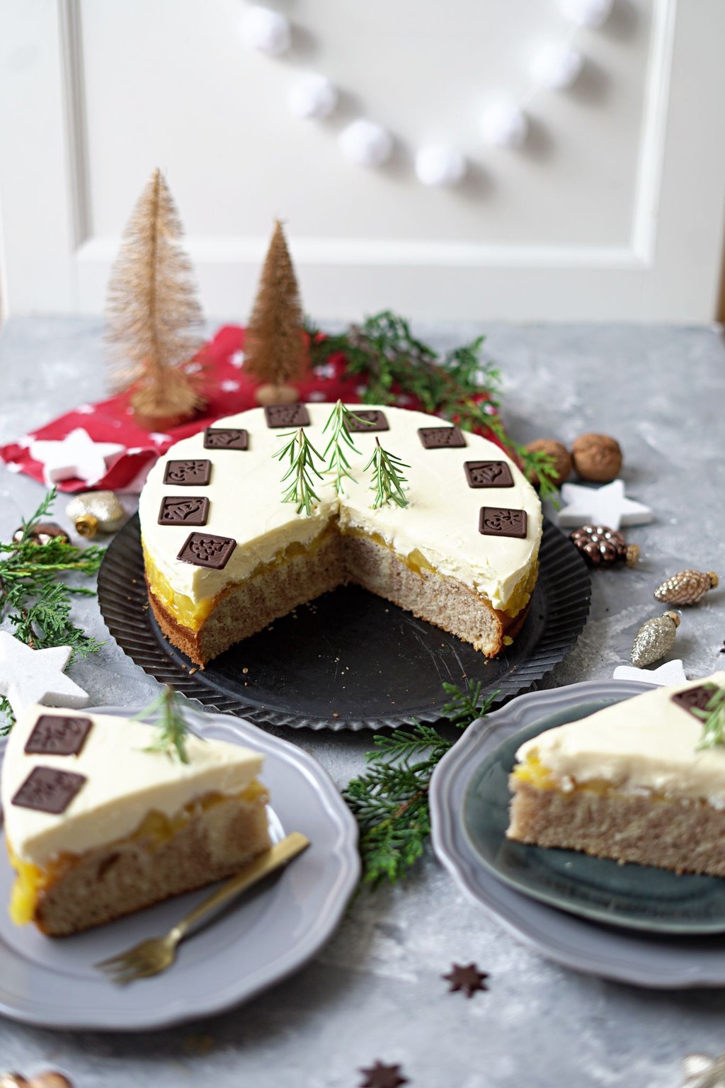 Schokodekor und Rosmarinzweige geben der Weihnachtstorte mit gestreiftem Boden und fruchtig-cremiger Füllung den letzten Schliff.