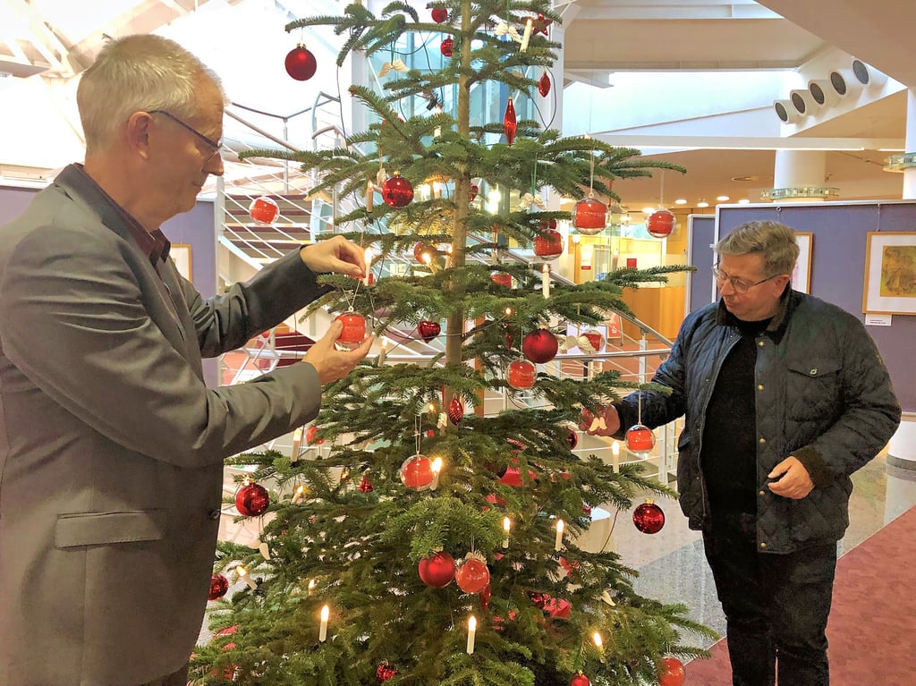 Detlef Kürten (l.) und Andreas Löbel hängen Kugeln für das Projekt Weihnachtsengel der Stiftergemeinschaft an den Weihnachtsbaum in der Geschäftsstelle der Harzsparkasse in Quedlinburg.