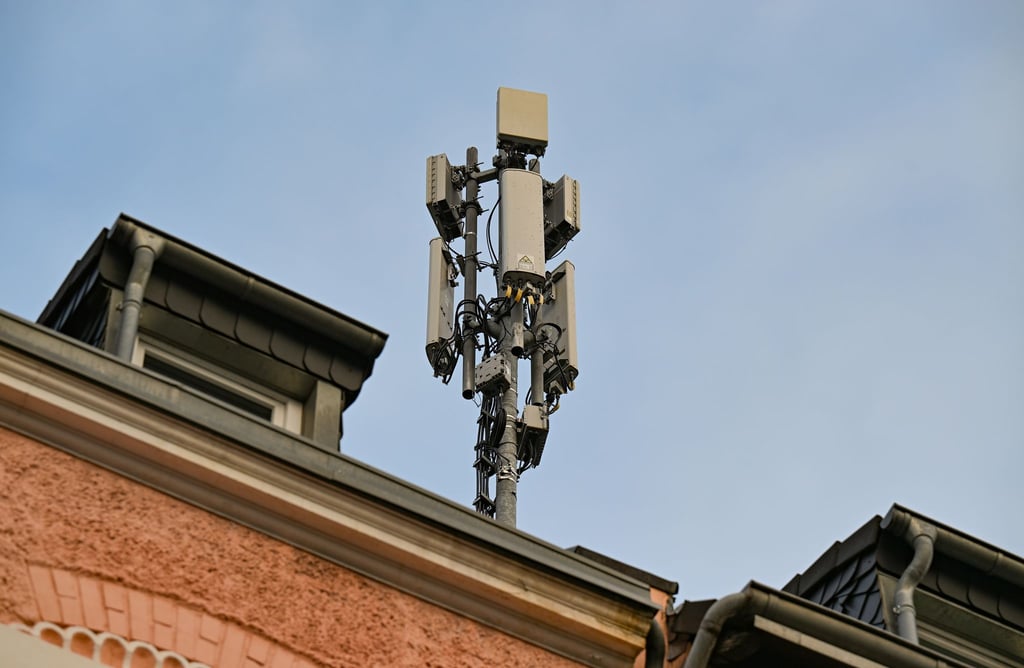 Ein Mobilfunkmast mit 4G/LTE-Antennen (länglich) und 5G-Antennen (quadratisch) steht auf einem Dach eines Wohnhauses.